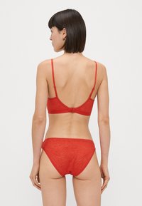 Conjunto de lencería de encaje rojo que incluye un sujetador con tirantes ajustables y una braguita a juego con un patrón texturizado. Se muestra la vista trasera.