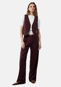 Gilet ajusté bordeaux et pantalon large, associé à un top blanc ajusté à manches courtes. Tissu lisse, boutons minimalistes, design épuré.