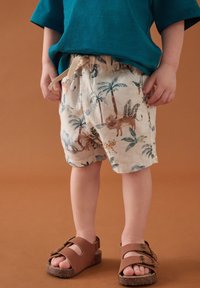 Shorts beige pour enfant avec imprimé d'animaux de la jungle et de palmiers. Taille élastique avec cordon de serrage. Sandales marron à boucles.