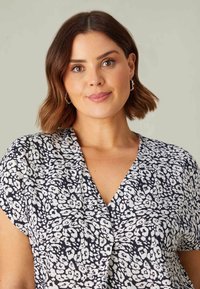 Vitt blommönster på en marinblå blus med v-ringning och korta ärmar. Slät textur med en avslappnad passform.