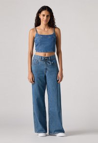 Top cropped de denim com alças finas, combinado com jeans de perna larga de cintura alta. Cor azul clara com uma textura suave e detalhes de costura mínimos.