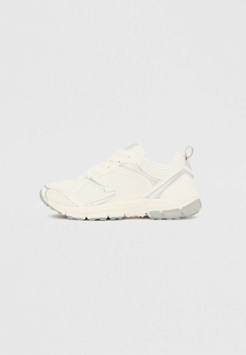 Pantof sport alb cu partea superioară texturată și accente gri deschis, cu vârf rotunjit și talpă flexibilă din cauciuc cu caneluri pentru tracțiune.