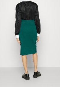 Teeleenvihreä lyijykynähame pehmeästä kankaasta, korkealla vyötäröllä ja valkoisilla sivuraitoja. Yhdistetty mustaan satiiniin oversized-toppiin ja mustiin kenkiin.