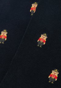 Tela azul marino con un patrón repetido de pequeños ositos de peluche vestidos como soldados de juguete con chaquetas rojas, pantalones negros y gorros con detalles dorados.