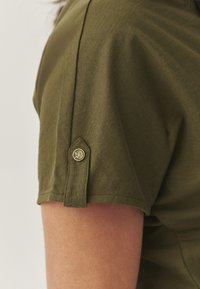 Olijfgroene katoenen t-shirt met korte mouwen en een knoopdetail, met een soepele textuur die de stiknaad op de schouder accentueert.