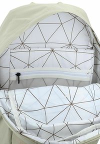 L'interno dello zaino verde chiaro presenta un tessuto bianco con un motivo geometrico di linee marroni. Include una tasca con zip e una sezione imbottita.