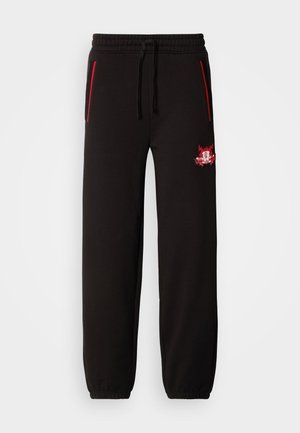 Black sweatpants with an elastic waistband, red accent zippers, and a prominent embroidered logo on the left thigh. Smooth texture, tapered fit.