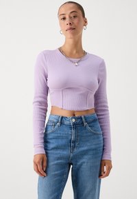 Top de cereja de manga longa canelado com silhueta ajustada e decote redondo, combinado com jeans de denim azul de cintura alta.