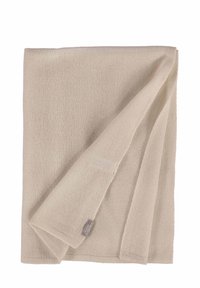 Couverture en tricot beige clair, pliée, avec une texture douce et une couture subtile, comportant une petite étiquette de marque dans le coin.