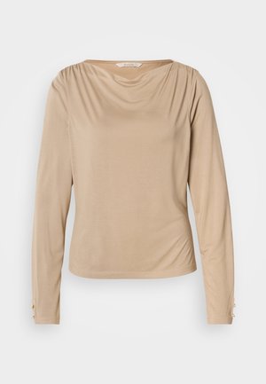 Beżowa bluzka z długim rękawem, o drapowanym dekolcie, gładkiej fakturze i ozdobna guzikami na mankietach, wykonana z miękkiego, elastycznego materiału.