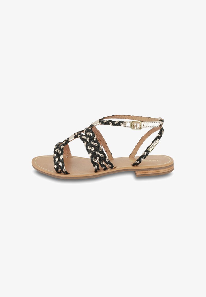 Sandales tressées noir et blanc avec une semelle plate en tan, dotées d'une fermeture à boucle et de brides texturées, idéales pour un usage décontracté.