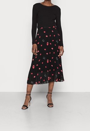 Sort plisseret nederdel med røde læbe- og læbestiftmønstre, parret med en tætsiddende sort langærmet top og sorte højhælede sandaler med remme.