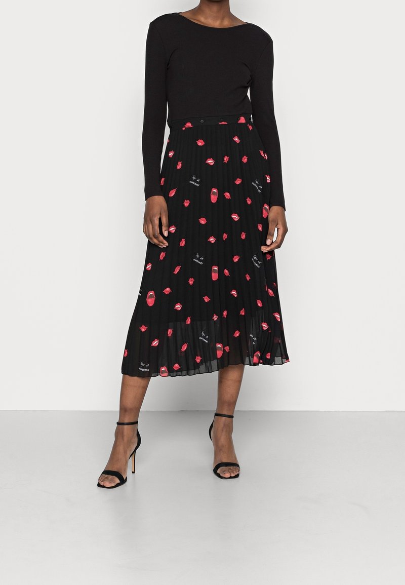 Zwarte geplooide rok met rode lippen en lippenstiftpatronen, in combinatie met een fitted zwarte langslovend top en geschenkte zwarte hoge hakken sandalen.