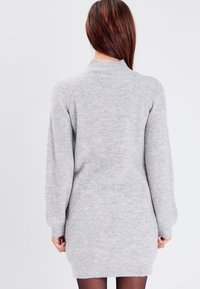 Robe-pull gris clair côtelée avec manches longues et col montant, présentant une maille texturée et une silhouette ajustée, arrivant à mi-cuisse.
