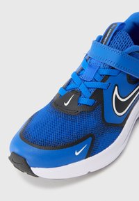 Blauwe sportieve schoen met een bovenwerk van mesh, zwarte en witte accenten, een gewatteerde kraag en een rubberen loopzool. Voorzien van veters en een klittenbandsluiting.