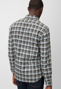 Langärmliges Karoshirt mit blauen, braunen und weißen Karomustern, mit einem Kragen und geknöpften Manschetten, von hinten gezeigt.