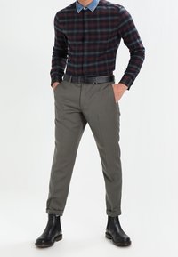 Gestreepte overhemd in donkerblauw en bordeauxrood, gecombineerd met grijze, slimfit broek. Zwarte leren Chelsea-laarzen maken de outfit compleet.