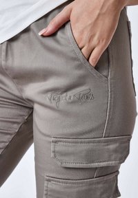 Pantaloni cargo grigi realizzati in tessuto morbido, con tasche laterali e logo ricamato "Project x Paris" vicino alla vita.