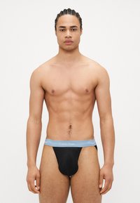 Crne tange donje rublje s mekanim, svijetloplavim pojasom na kojem je logotip Calvin Klein. Glatka tekstura i prilagođen dizajn.