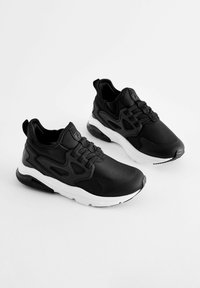 Des chaussures de sport noires au design élégant, avec une tige synthétique lisse, des semelles blanches, des lacets épais et des accents texturés.