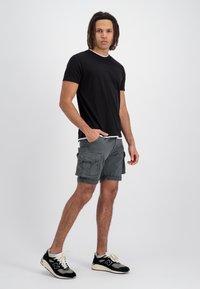 Un tricou negru cu mânecă scurtă și detalii albe, combinat cu o pereche de pantaloni scurți gri cu buzunare multiple. Purtați cu adidași negri și gri.