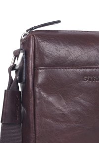 Borsa a tracolla in pelle marrone con superficie texturizzata, dotata di accessori in argento, tracolla regolabile e tasca frontale.