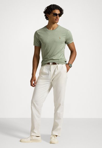 Πράσινο βαμβακερό μπλουζάκι με στρογγυλή λαιμόκοψη, συνδυασμένο με κρέμες παντελόνια και λευκά αθλητικά παπούτσια. Το μοντέλο φοράει γυαλιά ηλίου και στέκεται με τα χέρια στις τσέπες.