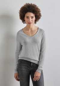 Ljust grått v-ringat tröja i mjukt tyg, med långa ärmar och ribbade manschetter och nederkant, stylad med mörkgrå jeans.