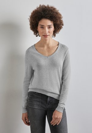 Lichtgrijze V-hals trui gemaakt van zachte stof, met lange mouwen en geribbelde manchetten en zoom, gestyled met donkergrijze jeans.