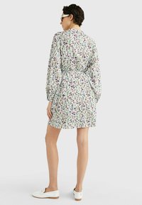 Abito con motivo floreale a maniche lunghe, vita stretta, sfondo bianco, fiori multicolori e vestibilità comoda, abbinato a scarpe bianche.