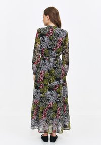 Long, flowing dress in sheer black fabric with floral patterns in green, purple, and red. Features long sleeves and a tiered hem.