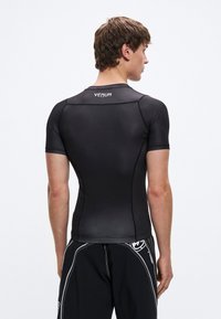 Μαύρο κοντομάνικο μπλουζάκι συμπίεσης μ�ε λεία υφή. Διαθέτει στρογγυλή λαιμόκοψη και το λογότυπο της Venum στο πάνω μέρος της πλάτης. Εφαρμοστή σχεδίαση.