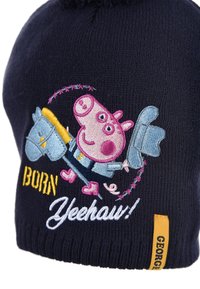 Navy knitted hat with a pom-pom, featuring embroidered pink character and text "BORN Yeehaw!" in yellow and white. Yellow label on side.