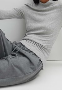 Grå ribbad polotröja med en figurnära design, i kombination med lösa, grå byxor med knytmidja och volangdetaljer vid fållarna.