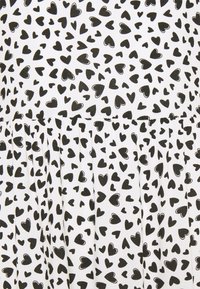 Biała tkanina z wzorem małych, rozmieszczonych czarnych serc. Materiał jest lekki i teksturowany, z marszczeniami przy dolnej części.