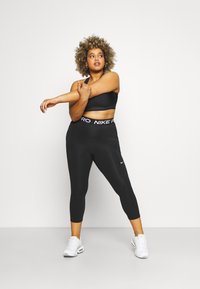 Musta urheiluliivi ja capri-legginssit, joissa on Nike Pro -vyötärö. Yhdistetty valkoisiin urheilukenkiin, korostaen tiukkaa muotoilua ja joustavaa kangasta.