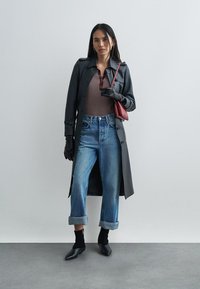 Μαύρο παλτό τρεντς πάνω από καφέ ριμπ μπλούζα, ξεθωριασμένο μπλε τζιν με γυρισμένα μανίκια, μαύρα γάντια και μια μικρή κόκκινη τσάντα. Μαύρα παπούτσια με τακούνι.