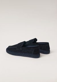 Mørkeblå ruskind loafers med en flet sål, der har en frontklap og minimale syninger, hvilket giver en elegant og glat tekstur.