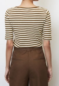 Pruhovaný hnědý a krémový top s kulatým výstřihem, krátkými rukávy a volným střihem, doplněný hnědými kalhotami s vysokým pasem a kapsami.