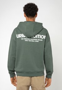 Grüne Kapuzenjacke mit einem großen weißen Textlogo auf dem Rücken, aus weichem Stoff gefertigt, mit einer Kängurutasche und einer verstellbaren Kapuze.