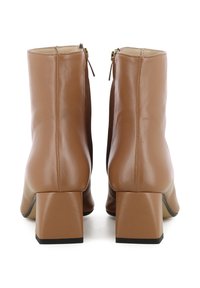 Bottines en cuir marron avec un talon carré, présentant une finition lisse et une fermeture éclair sur le côté. Les semelles ont un accent noir.