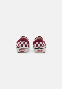 Červenobiele kockované slip-on topánky s plátenným zvrškom a gumovou podrážkou. Obsahujú jemné prešitie a klasické logo Vans na päte.