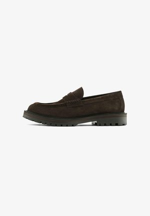 Mocassins en daim marron avec une semelle basse, présentant un design cousu et une finition lisse. Accentués par une bande décorative sur le dessus.