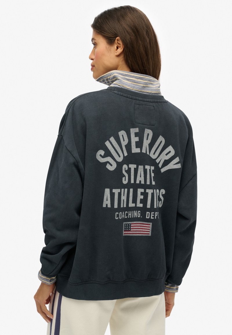 Felpa blu navy scuro con vestibilità oversize, con la scritta "Superdry State Athletics" stampata sul retro e dettagli a righe sul colletto. Materiale di cotone.
