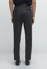 Grijze broeken met een slim fit, voorzien van twee achterzakken, subtiele stiksels en gedragen met zwarte dresschoenen. Glad stoftextuur.