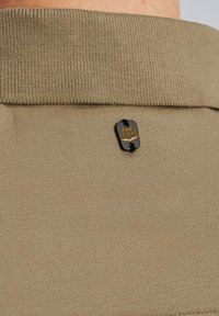 Beige gebreide polo met een zichtbare zwarte label met de tekst "PME LEGEND." De stof lijkt glad met een geribbelde textuur bij de kraag.