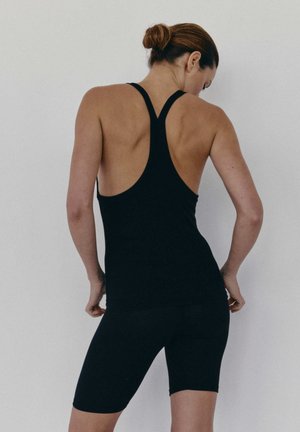 Czarna koszulka na ramiączkach z designem typu racerback, zestawiona z czarnymi szortami rowerowymi. Wykonana z gładkiego, elastycznego materiału. Posiada dopasowany krój.