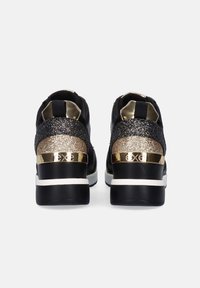 Zapatillas negras con un acento en el talón que brilla en dorado y plateado, con un diseño elegante y una entresuela blanca en contraste. Parte superior de tela texturizada.