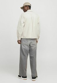 Hellbeige, langärmlige Hemdjacke mit geradem Schnitt; kombiniert mit lockeren, verwaschenen grauen Jeans und schwarzen Sneakers mit weißen Sohlen.