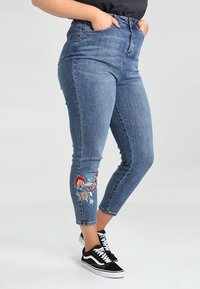 Džíny s vysokým pasem v modré denimové barvě se slim fit střih, s barevným květinovým vyšíváním na levém kotníku a klasickým pětivreckovým designem.